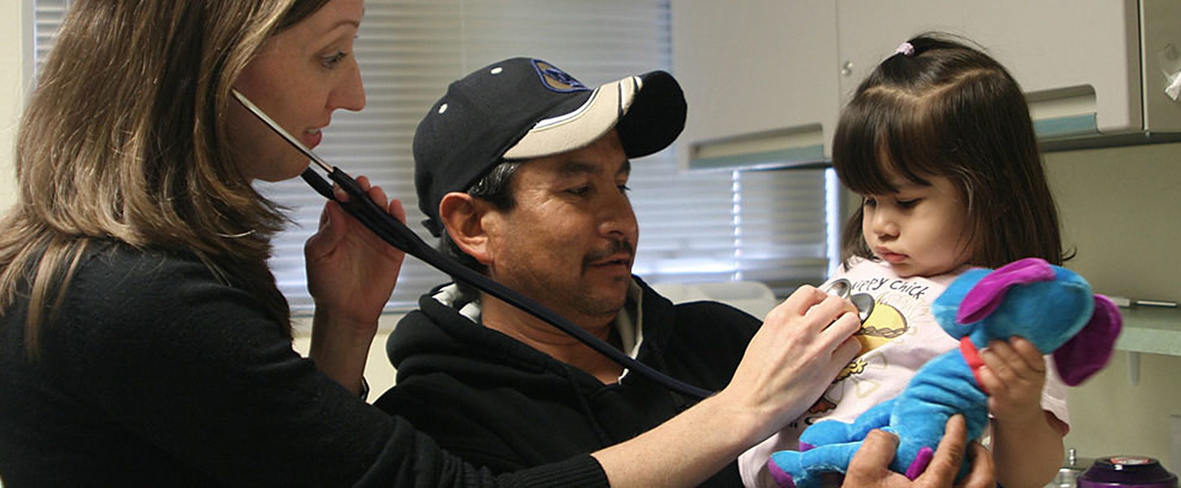 A clinician examining a young child held by her father during a check-up