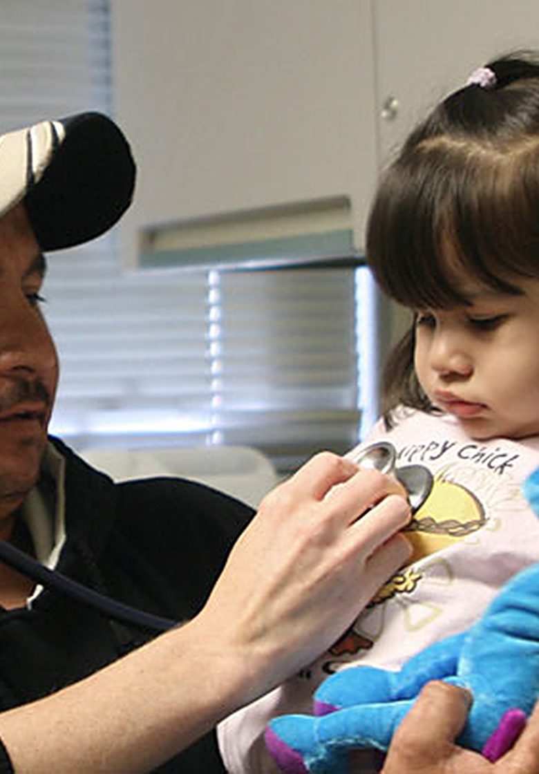 A clinician examining a young child held by her father during a check-up