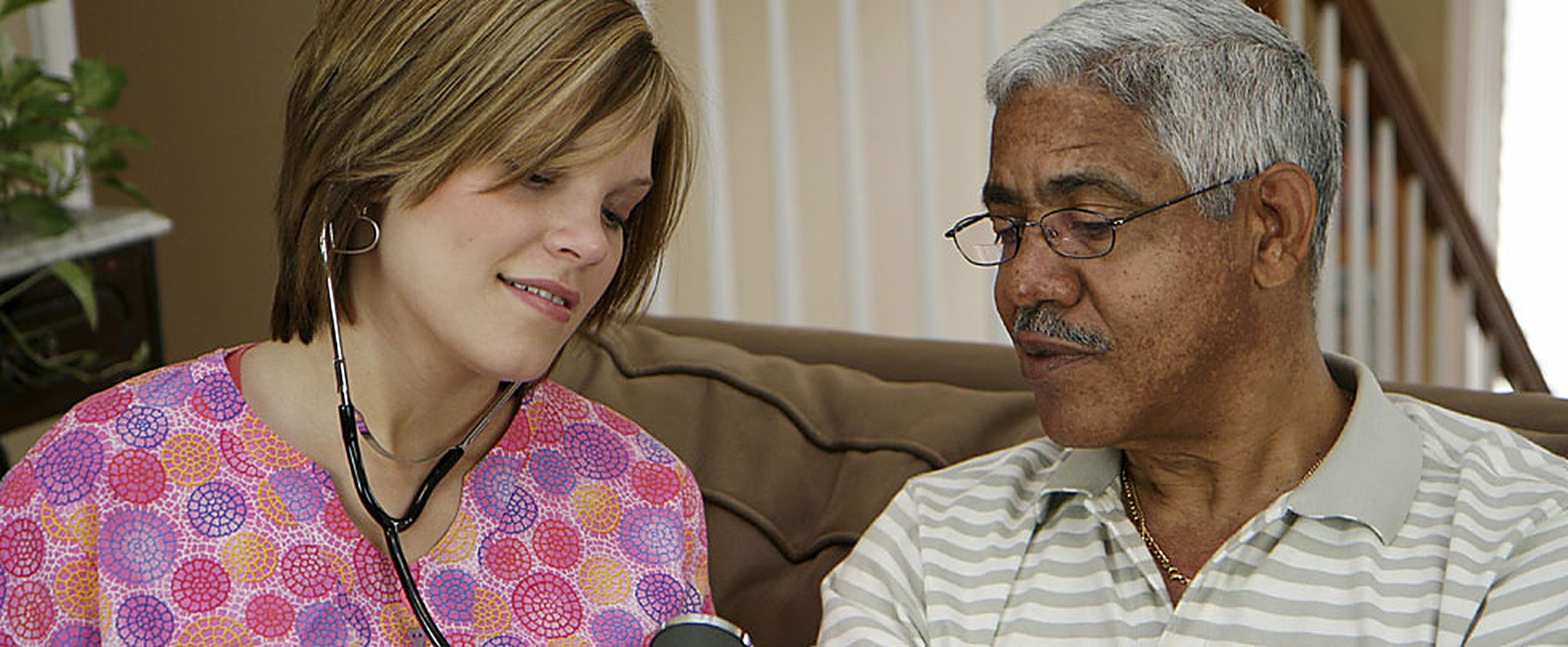 A nurse listening to an older patient's heart during a home visit
